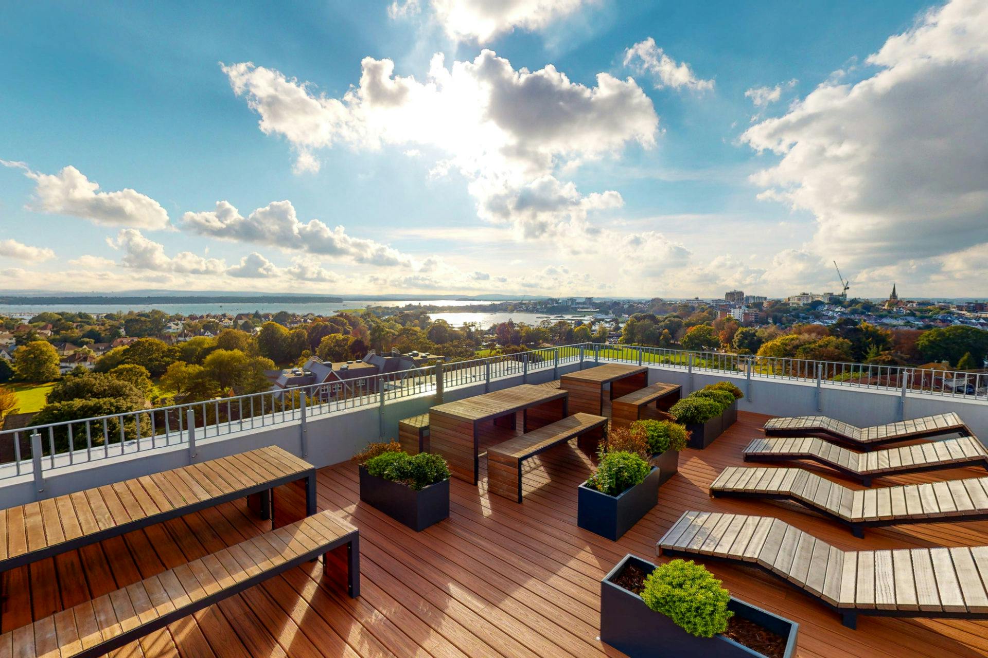 Rooftop terrace with wooden benches and planters, offering a panoramic view of a scenic landscape with a lake.
