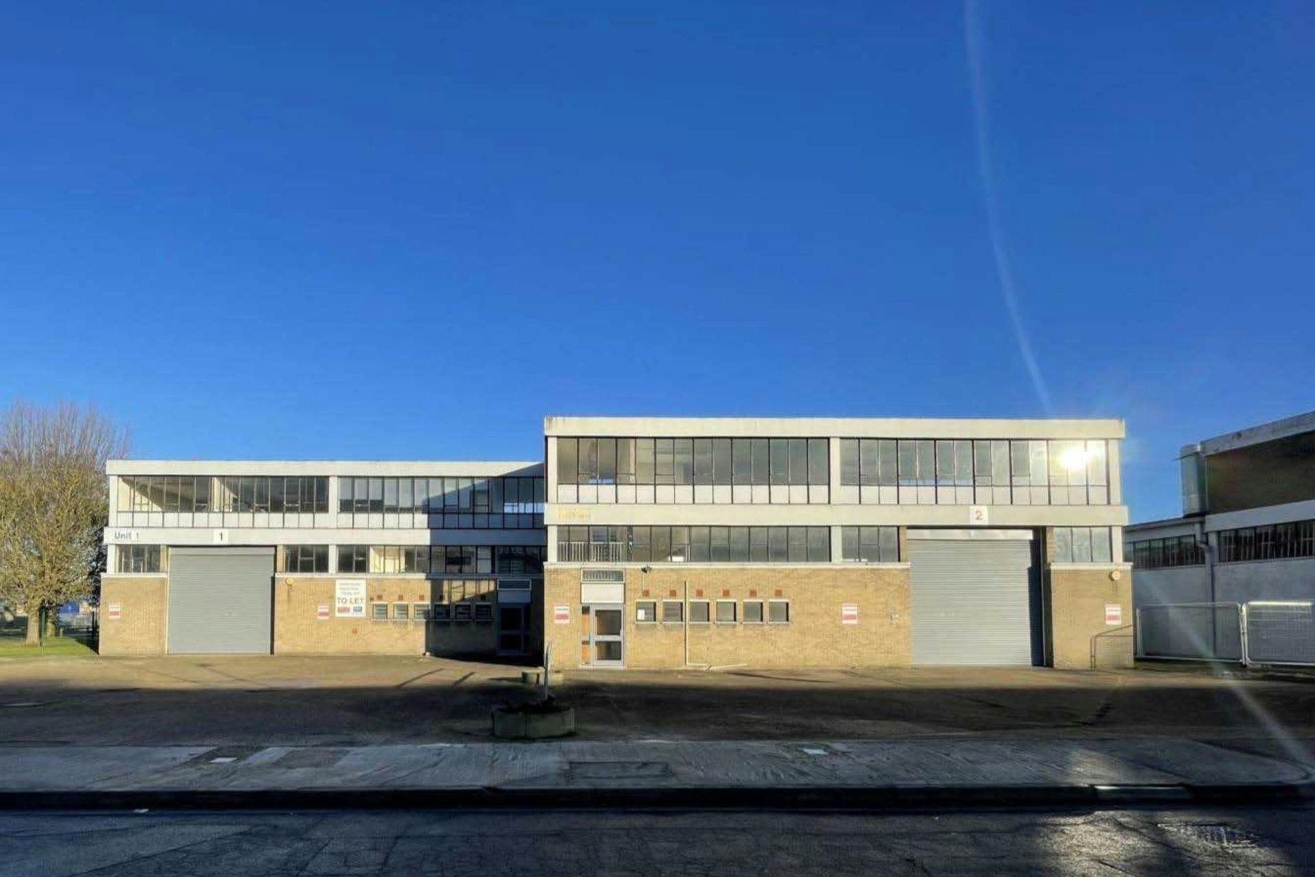 Industrial building with roller shutter doors, a two-storey office section with large windows, and clear blue sky above.